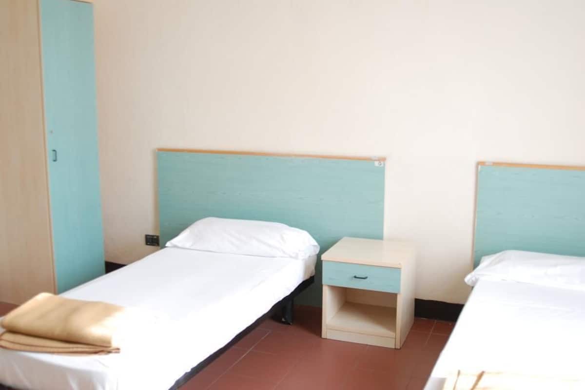 Una habitación con dos camas individuales, cada una con cabecero de madera y una mesita de noche con cajón.