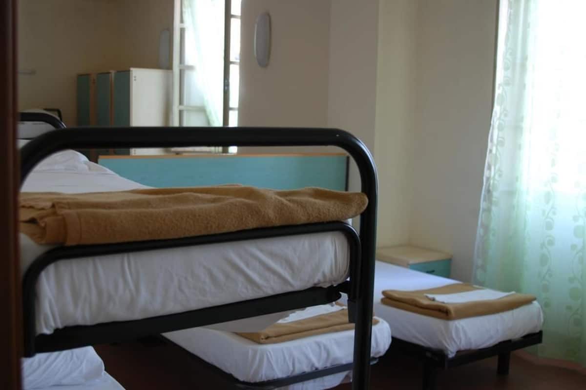 Una habitación con dos literas, una mesita de noche pequeña y una ventana con cortinas.