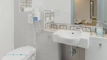 A modern bathroom with a white toilet, a sink with a mirror above it, and a small trash bin.