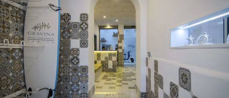 A hallway with patterned tiles, a surfboard, and a reception area with a scooter.