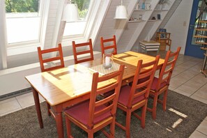Ruokailutila, jossa on puinen pöytä ja tuolit, maljakko, jossa on kynttilä, ja suuret ikkunat, joista on näkymä ulos.