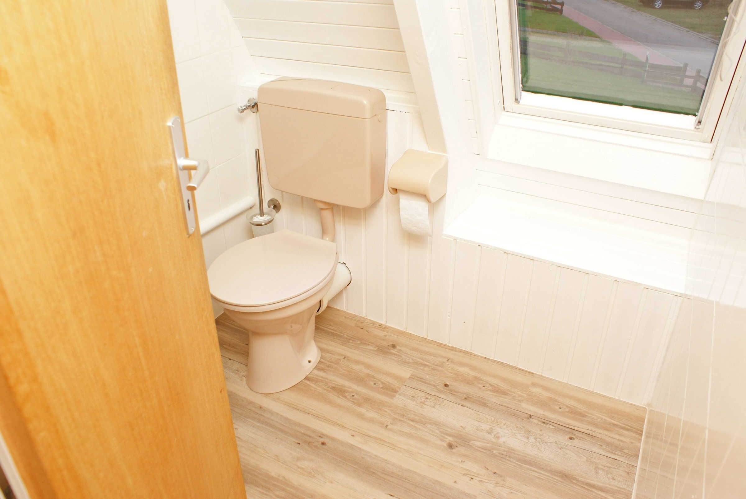 A small, clean bathroom with a toilet, wooden floor, and a window.