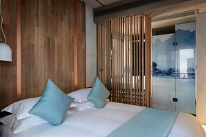 Habitación de hotel moderna con pared de madera, cama con ropa de cama blanca y almohadas color turquesa, y puerta de vidrio corrediza que da a un balcón con vista a la montaña.