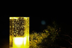 Una vela encendida en un recipiente de vidrio, con un fondo desenfocado.