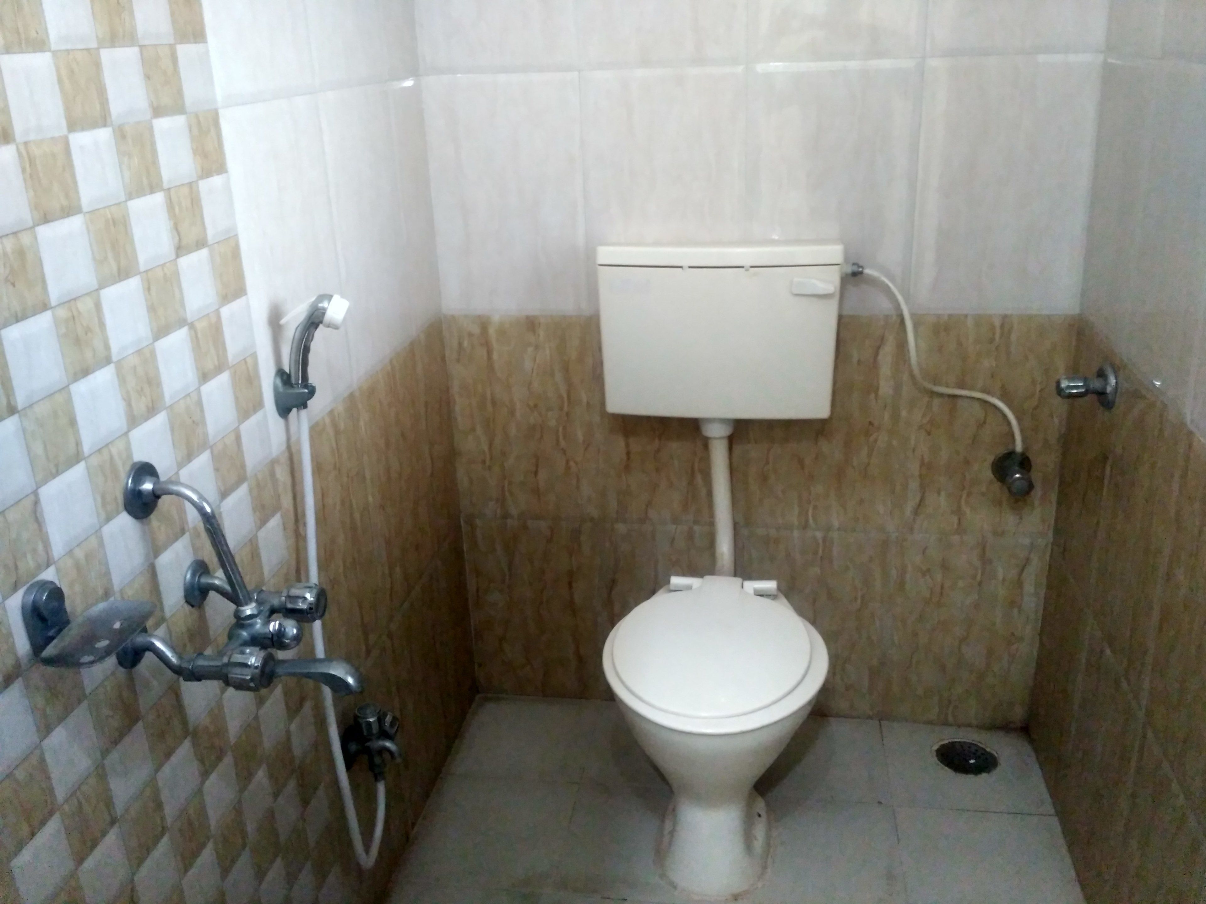 Et lille badeværelse med fliser, toilet, brusebad og håndvask.
