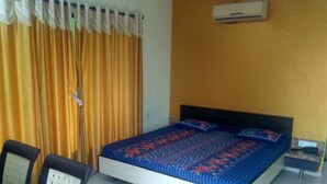 Un dormitorio con cama, dos sillas, aire acondicionado en la pared y una cortina.