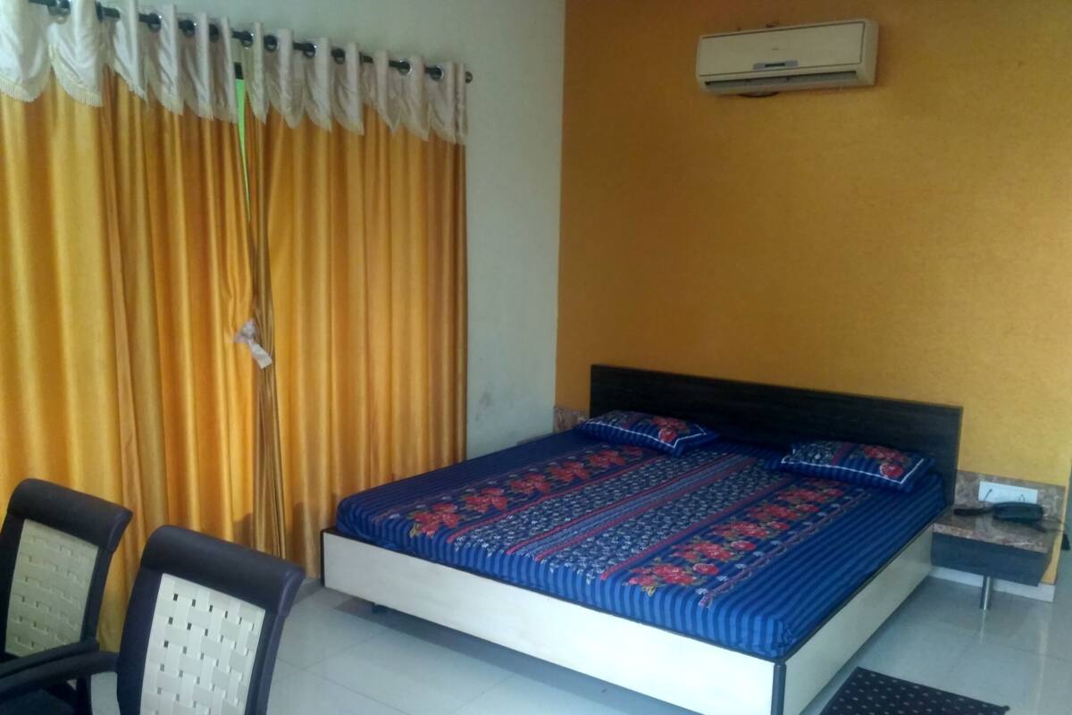 Un dormitorio con cama, dos sillas, aire acondicionado en la pared y una cortina.