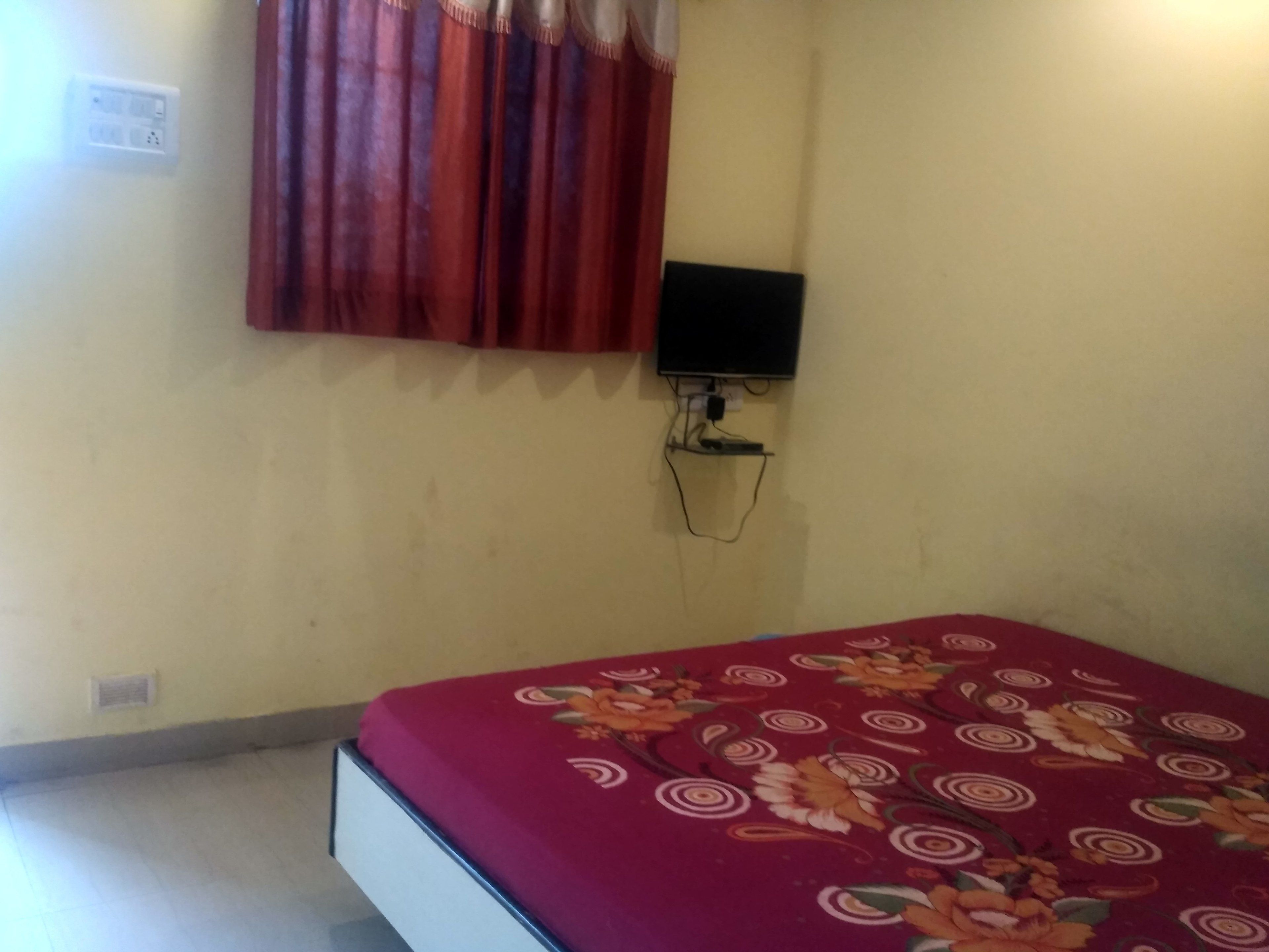 A room with a bed, a wall-mounted TV, and a power outlet.