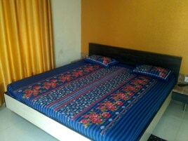 Una cama con cubrecama y almohadas de estampado floral, cabecera de madera y pared amarilla.