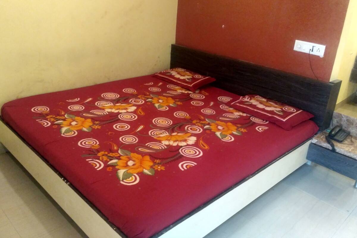 Una cama con colcha y almohadas estampadas con motivos florales, cabecera oscura y un enchufe de pared.