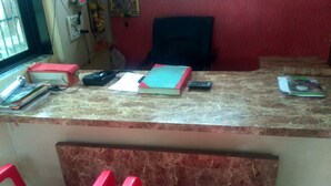 Un mostrador de recepción con encimera de mármol, sillas de plástico rojo y diversos objetos como libros y un teléfono.