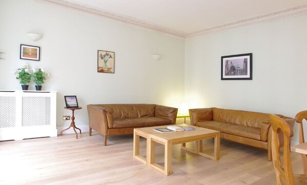 A living room with a brown leather sofa, a wooden coffee table, and a white cabinet with a small table beside it.