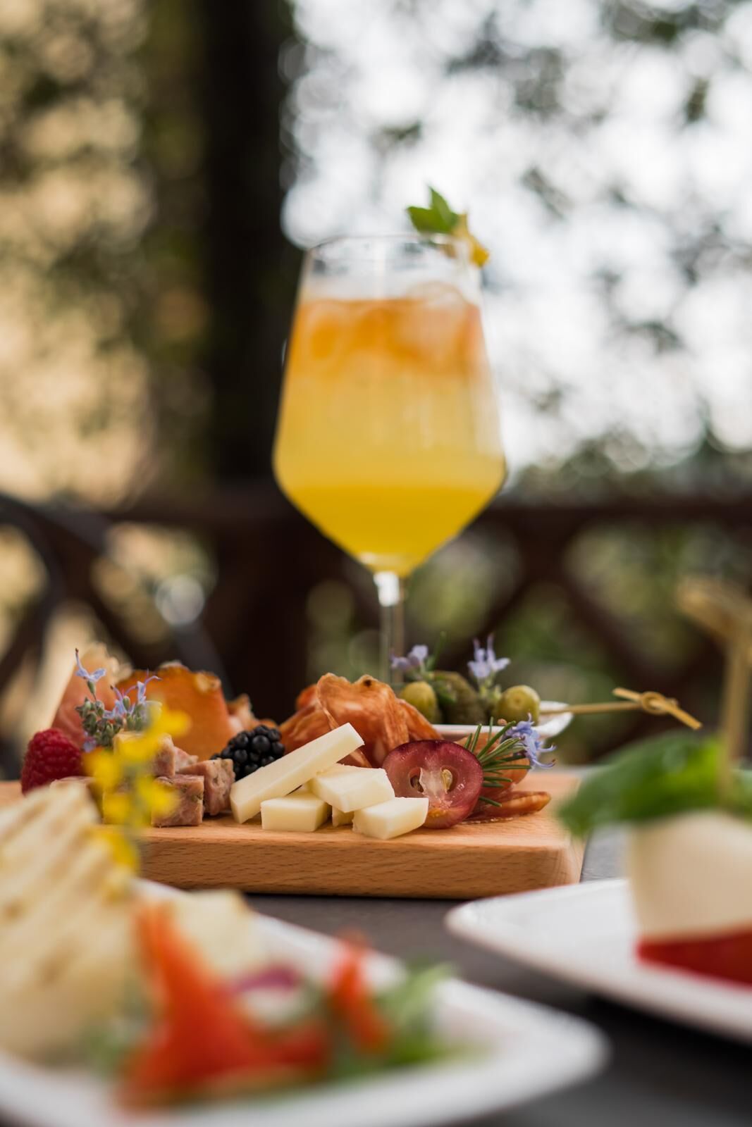 A charcuterie board with various cheeses, fruits, and a glass of orange juice.