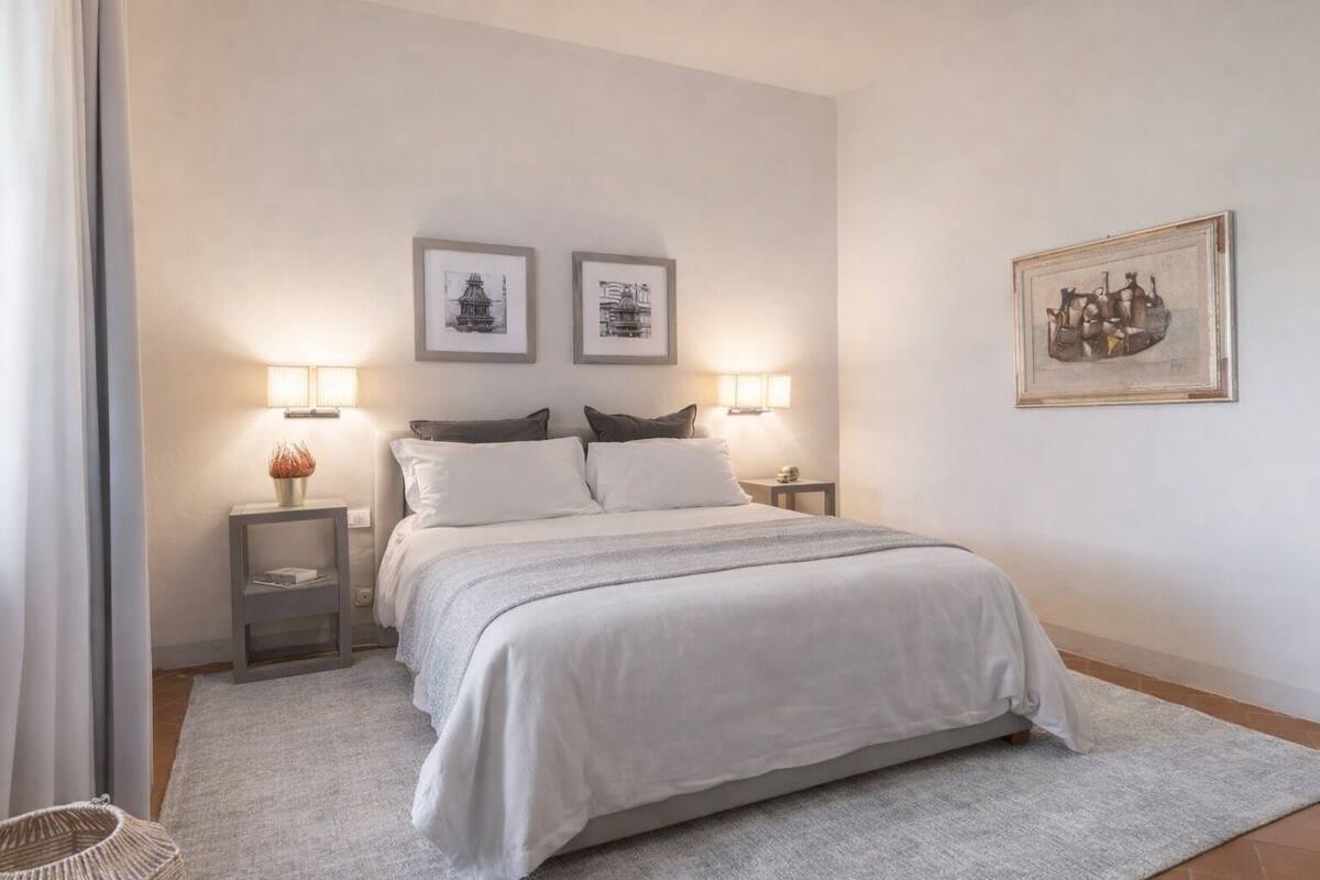 A neatly arranged bedroom with a bed, two bedside tables, a lamp, and framed artwork on the wall.