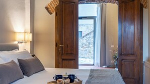 A hotel room with a bed, a tray with pastries, and a view of a stone building through open doors. - Borgo Iesolana Country Retreat (Bucine)
