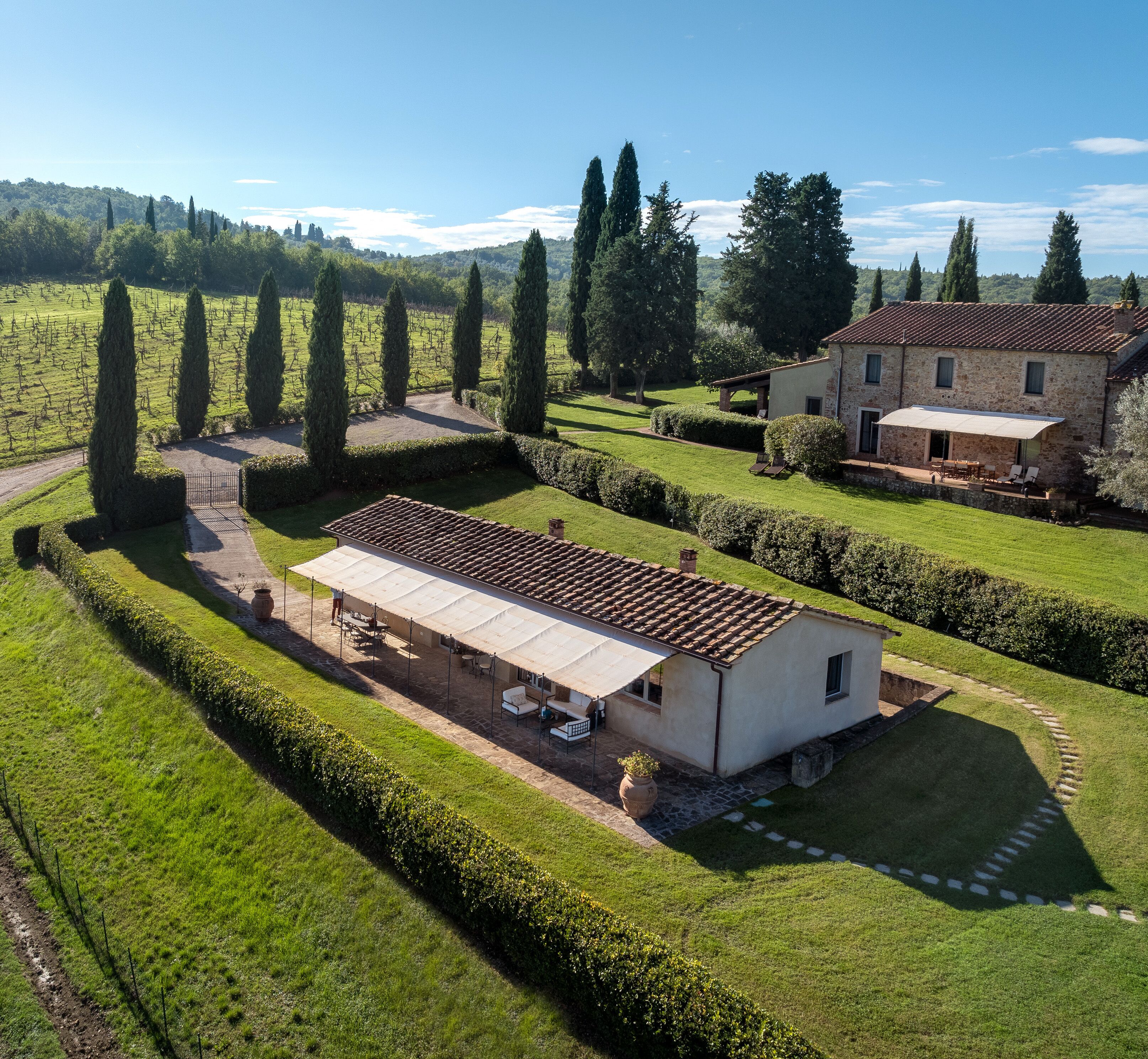 A large, single-story building with a tiled roof, surrounded by well-maintained hedges and a vineyard.