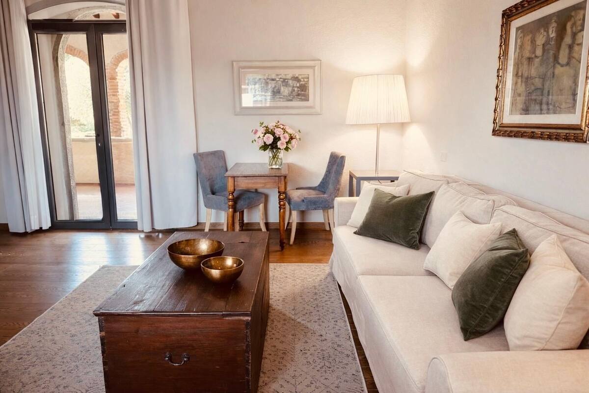 A living room with a sofa, a coffee table with bowls, two chairs, a lamp, and a painting on the wall.