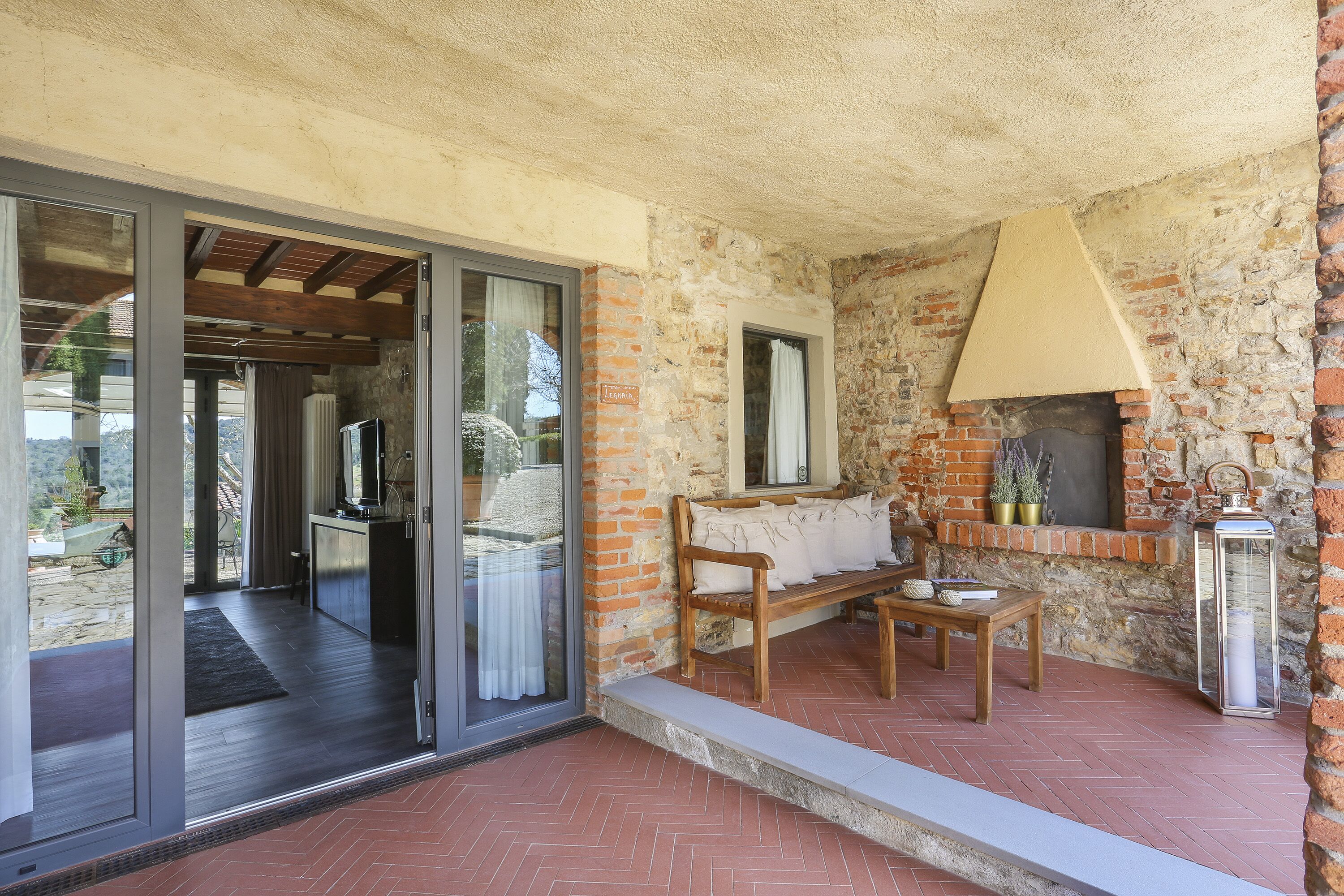 A cozy patio area with a stone wall, a wooden bench, a table, and a lantern.