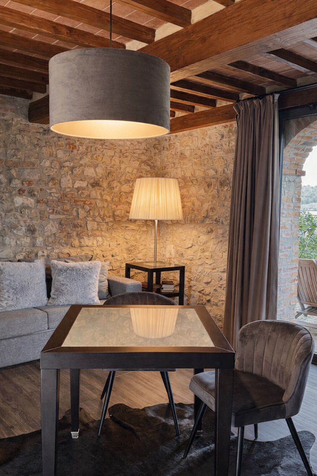 Una habitación acogedora con pared de piedra, techo de madera, una mesa con sillas, una lámpara y un sofá.