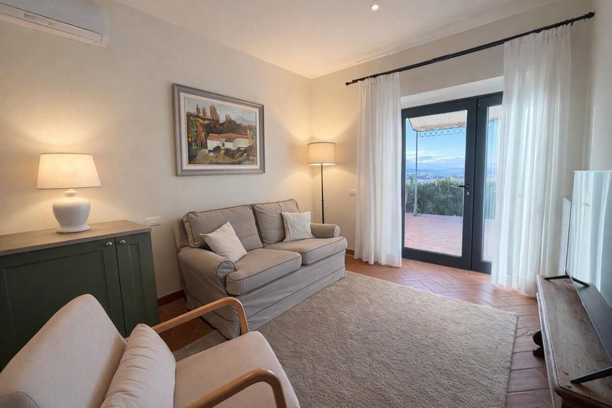 A living room with a sofa, two lamps, a painting, and a view through a glass door.