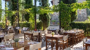 An outdoor dining area with wooden tables and chairs, surrounded by greenery and stone walls. - Borgo Iesolana Country Retreat (Bucine)