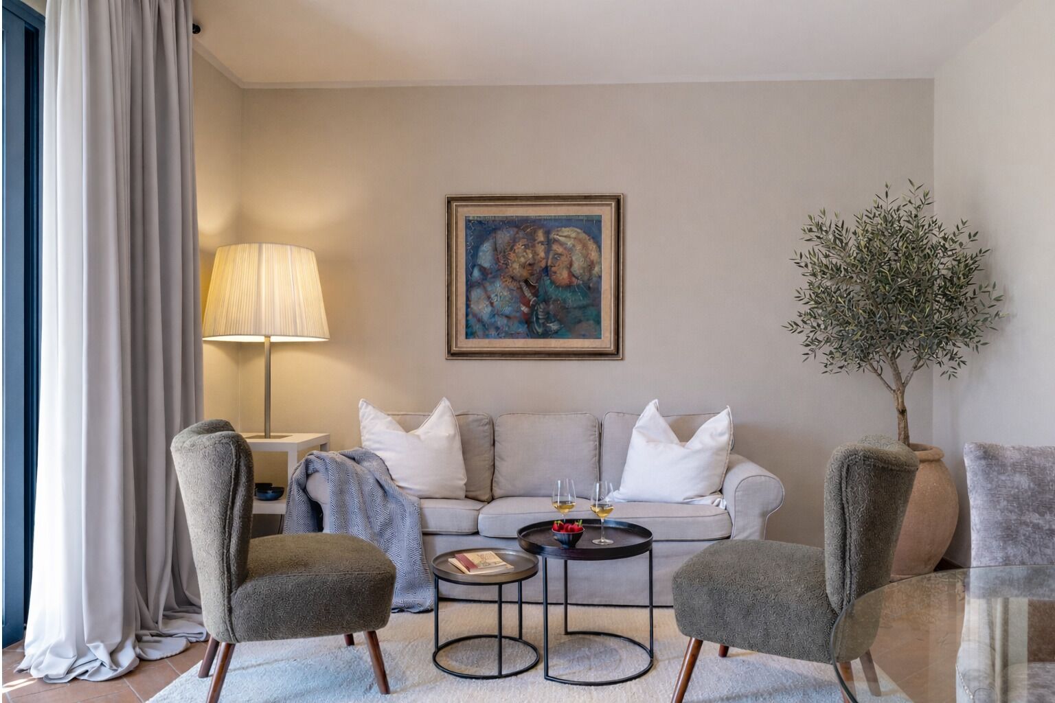 Ein modernes Wohnzimmer mit einer Couch, zwei Sesseln, einem Couchtisch, einer Lampe, einem Gemälde und einer Topfpflanze.