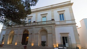 Ein Gebäude mit einer symmetrischen Fassade, Rundbogenöffnungen und einem Balkon mit Geländer.