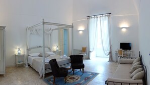 Ein Schlafzimmer mit Himmelbett, einer Sitzecke inklusive Sofa und Sesseln, einem Fernseher und einem kleinen Schreibtisch.