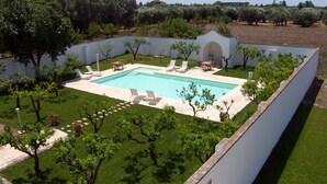 Ein rechteckiger Pool mit Liegestühlen und einem Tisch, umgeben von einer weißen Mauer und Bäumen.