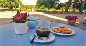 Een tafel met een glas ijsthee, een bord donuts en een bloevas.
