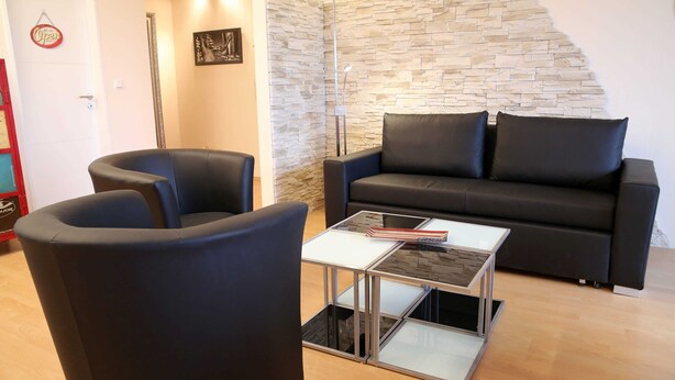 Uma sala de estar moderna com uma parede de pedra, um sofá de couro preto, uma mesa de centro de vidro e uma poltrona preta.