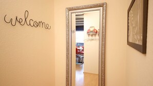 Um corredor com uma placa de 'welcome', um espelho e uma cadeira vermelha ao fundo.