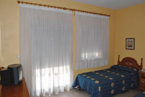 A room with a bed, a wooden headboard, a nightstand, a television, and curtains.