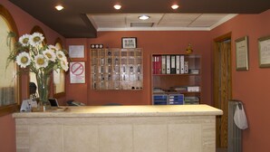 A reception desk with a vase of flowers, a bulletin board with notices, and a filing cabinet with binders. - Rey Teodomiro (Orihuela)
