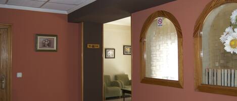 A hallway with a wooden door, a framed picture on the wall, and a window with a flower arrangement.