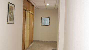 A hallway with beige tiled flooring, a wooden wardrobe, and two framed pictures on the walls.
