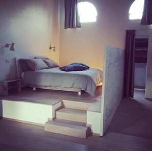 A bedroom with a bed, a small table, and a staircase leading to an upper level. - B&B Relais Druda (Cagli)