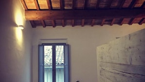 A room with a wooden ceiling, a window with patterned curtains, and a wall with a textured finish. - B&B Relais Druda (Cagli)