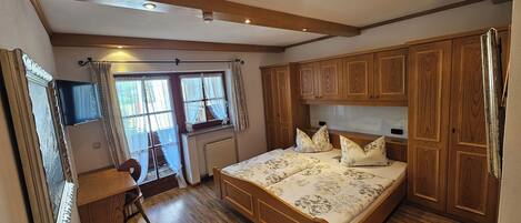 Un dormitorio con una cama de madera, una ventana con cortinas, un radiador y armarios de madera.