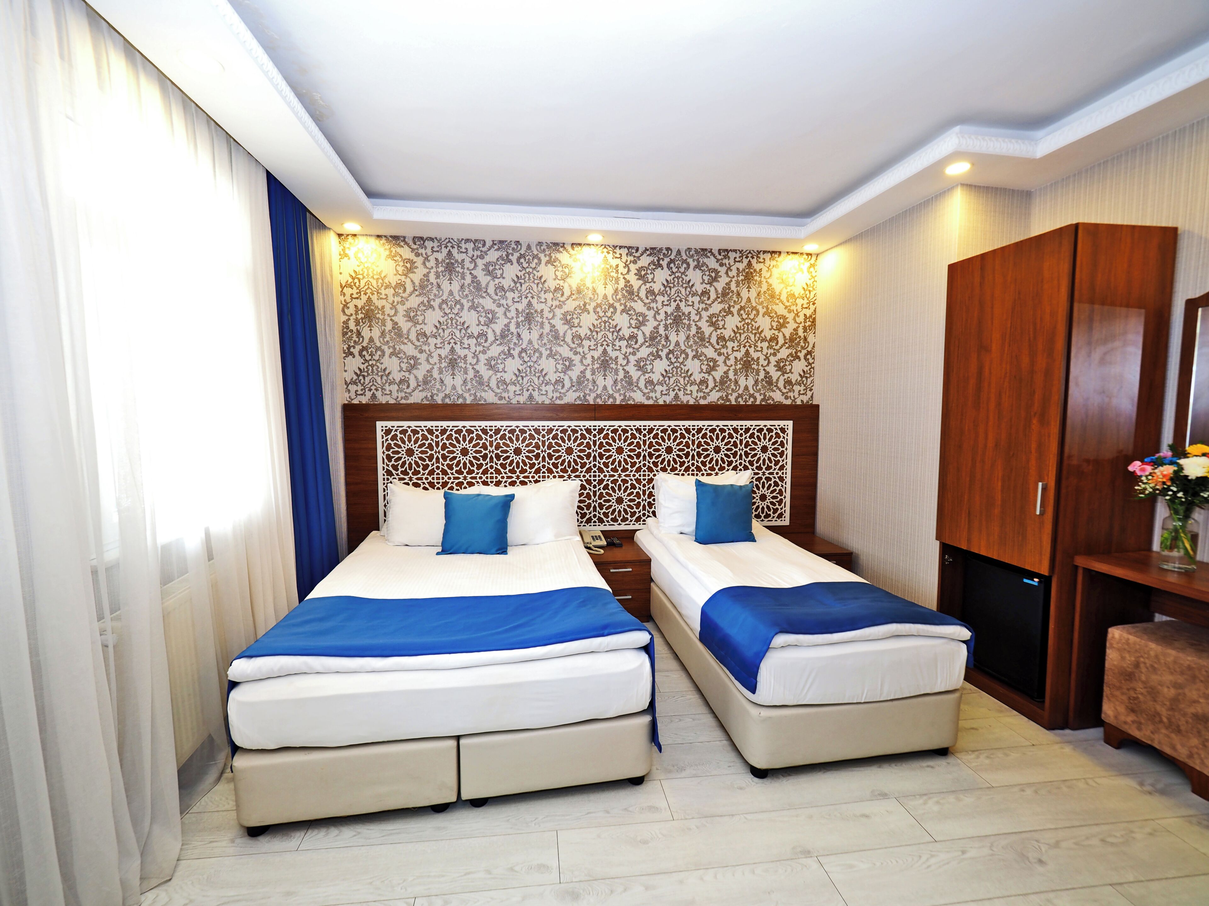 A hotel room with two beds, a wooden headboard, a wardrobe, and a nightstand.