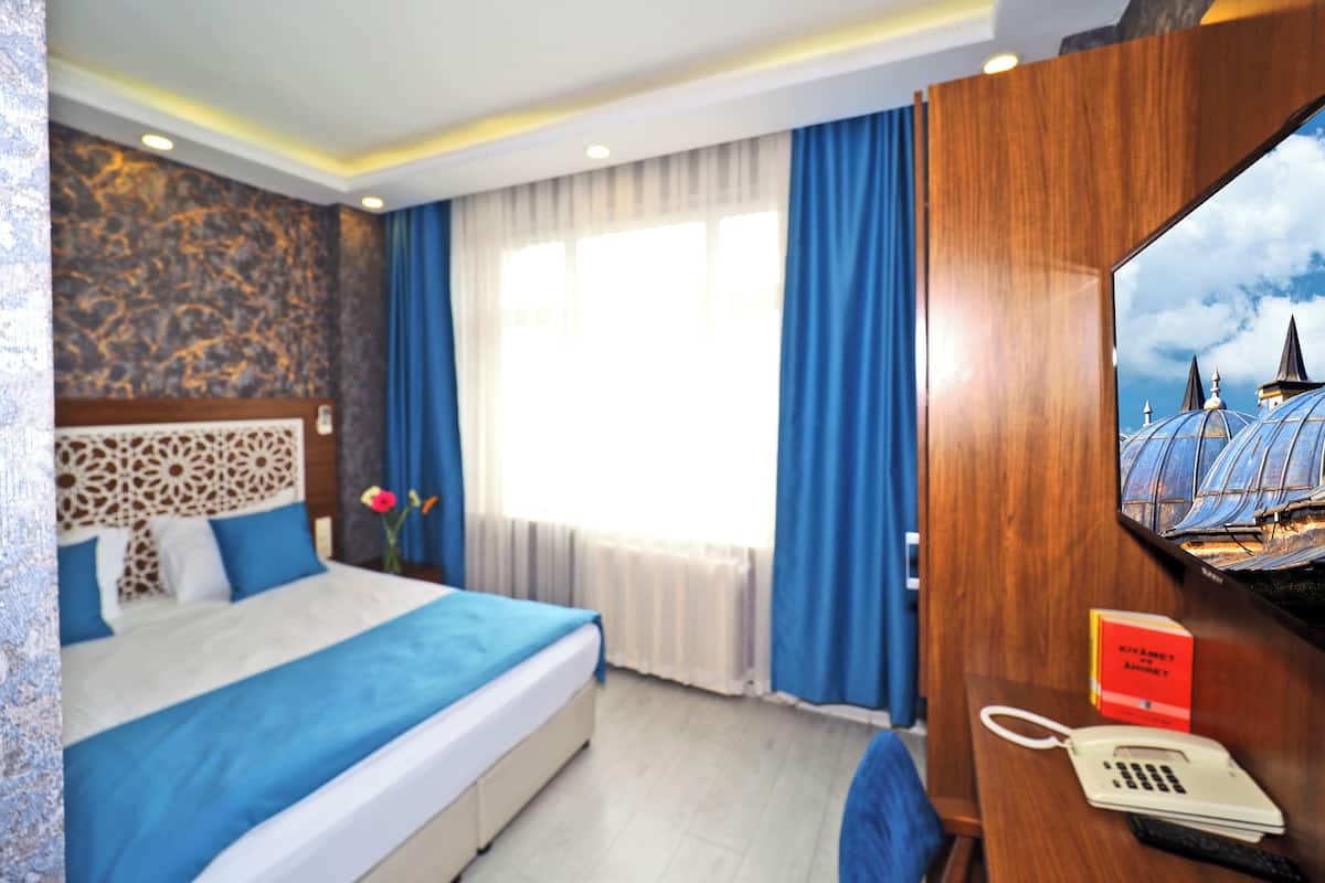 A hotel room with a bed, a desk with a telephone and a book, a window with curtains, and a wall with a decorative pattern.