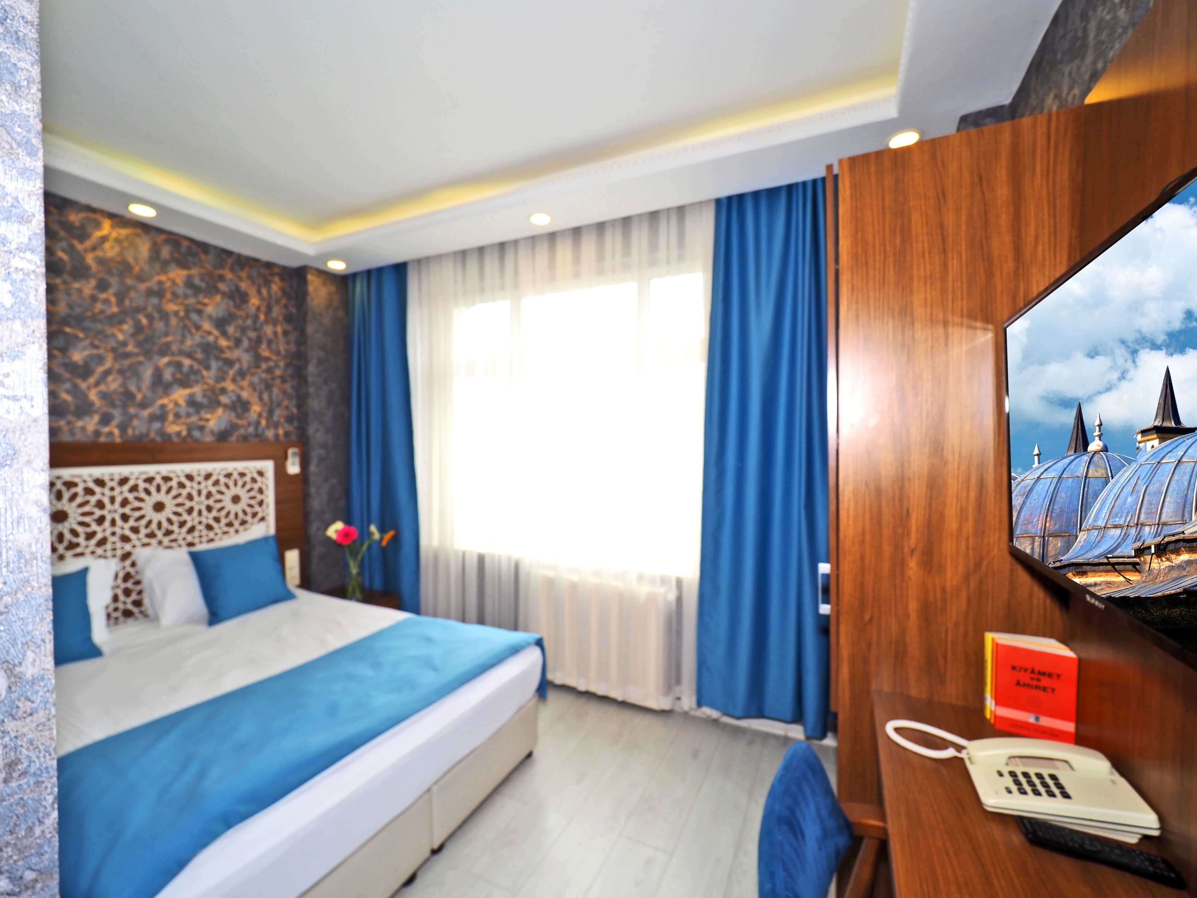 Una camera d'albergo con un letto, una scrivania con il telefono, uno specchio e una finestra con tende.