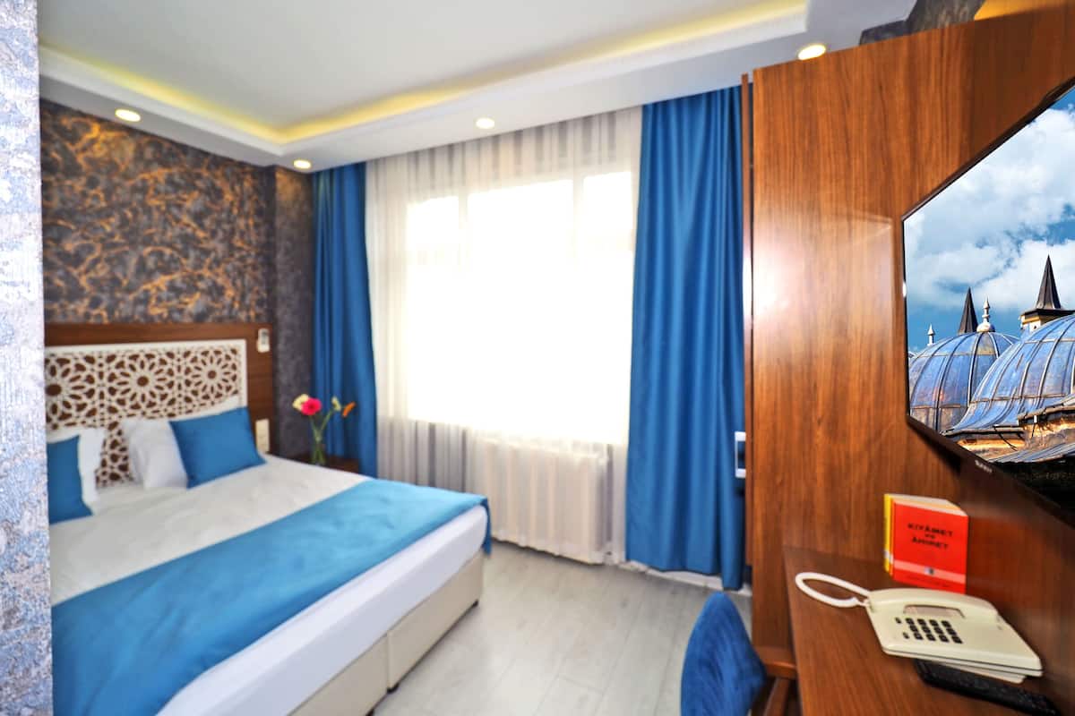 A hotel room with a bed, a desk with a telephone, a mirror, and a window with curtains.