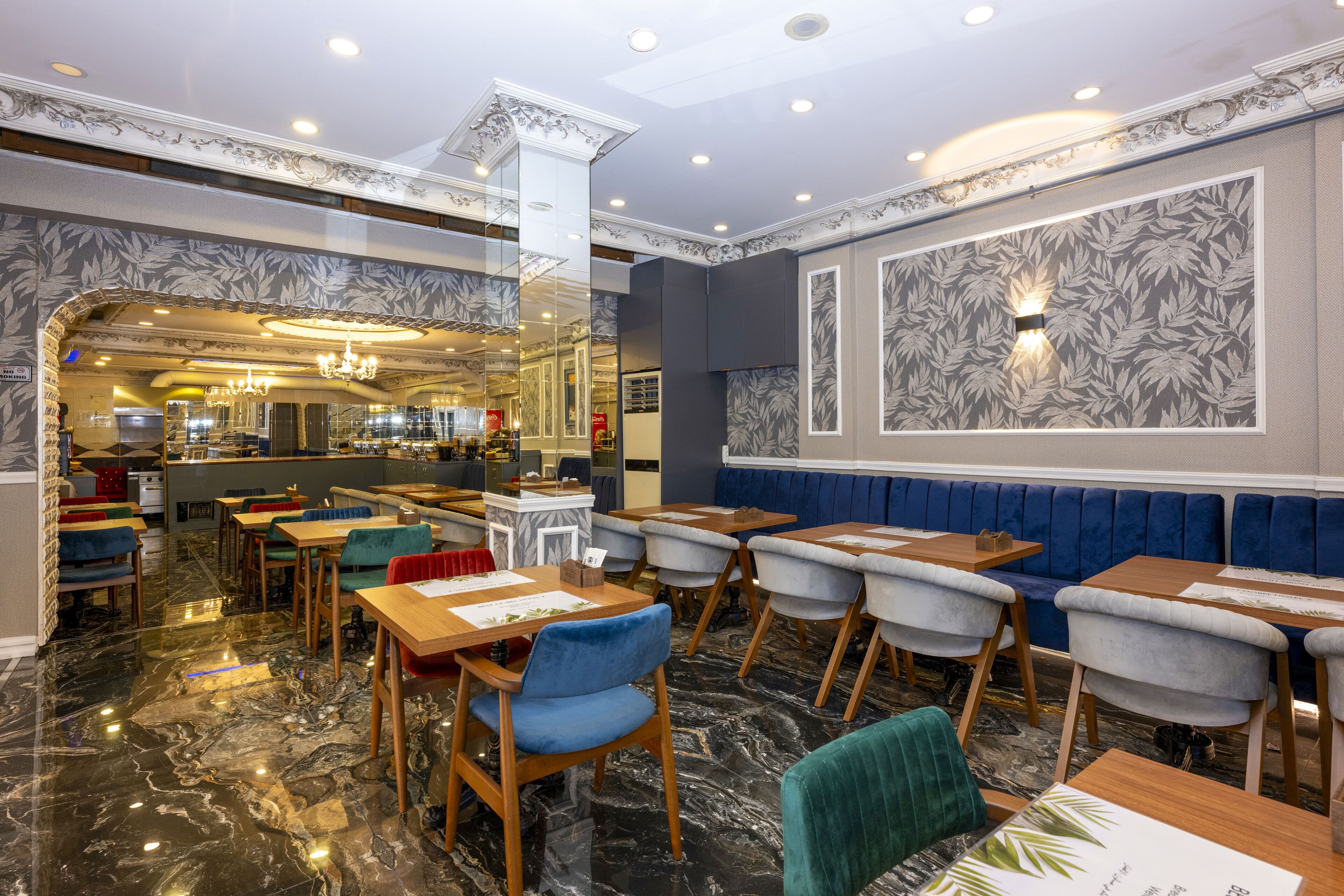 A restaurant with marble flooring, blue and grey upholstered booths, wooden tables, and a chandelier.