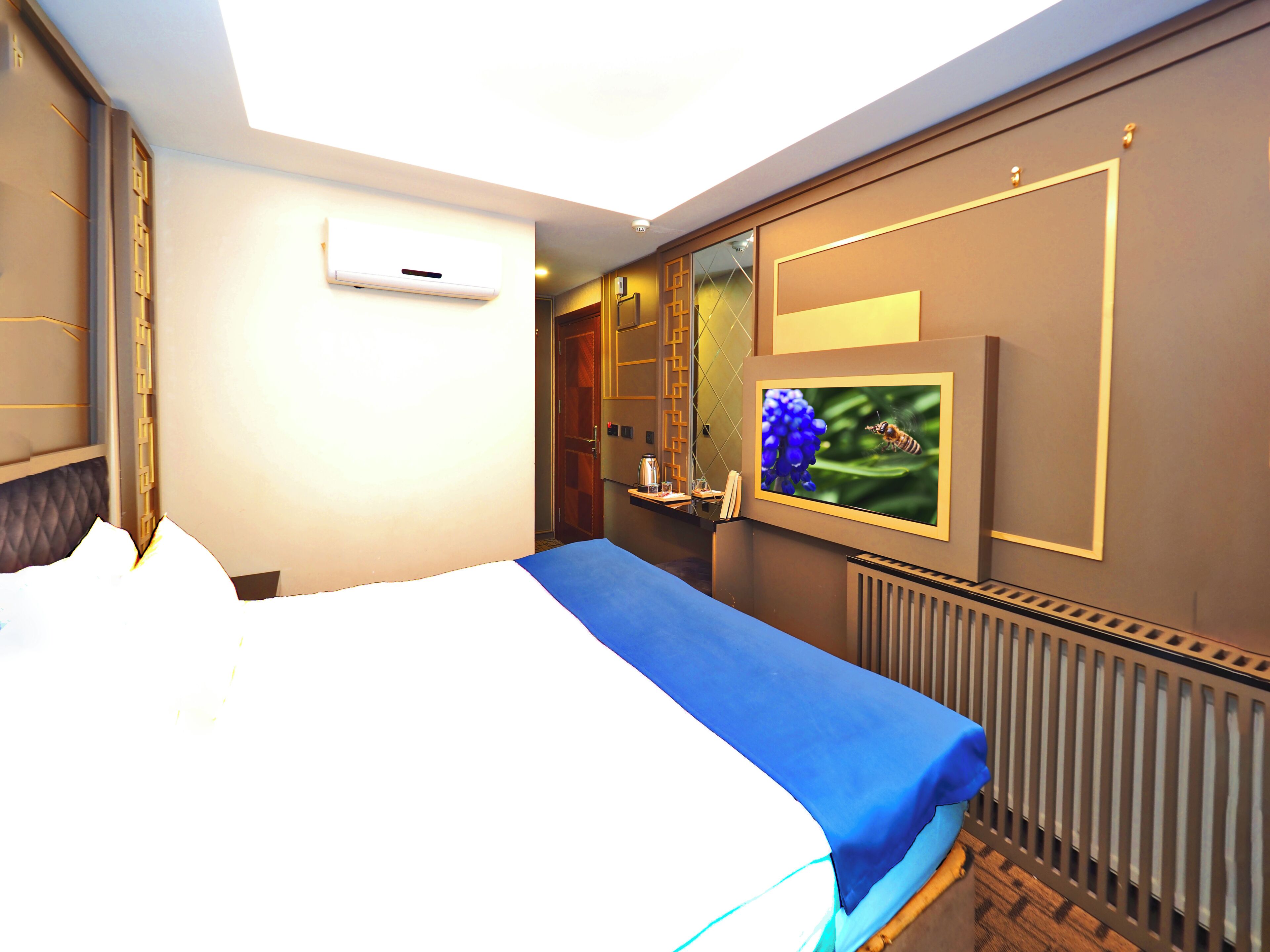 Una habitación de hotel con cama, televisión montada en la pared, ventana y radiador.