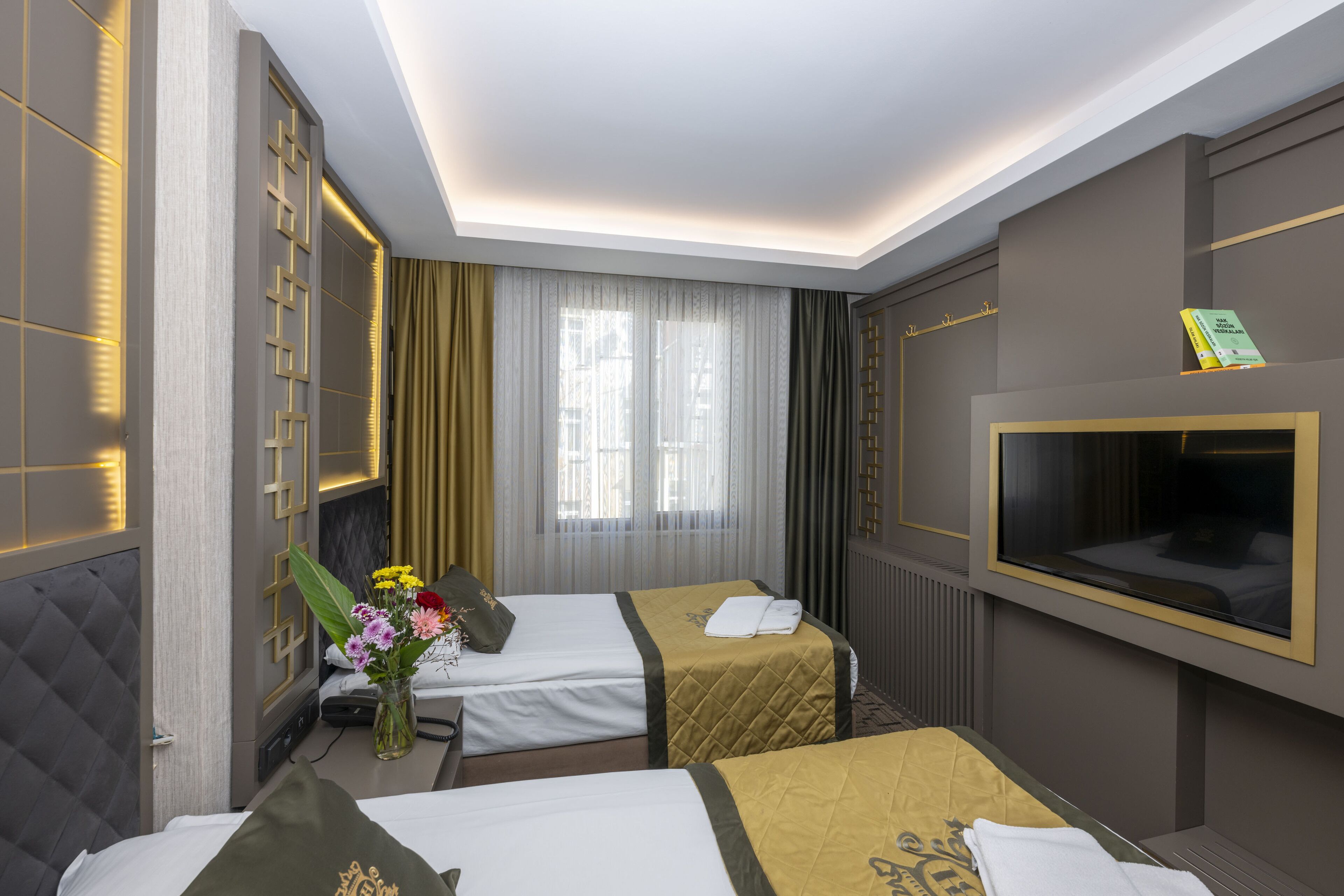 A hotel room with two beds, a TV mounted on the wall, and a large window with curtains.