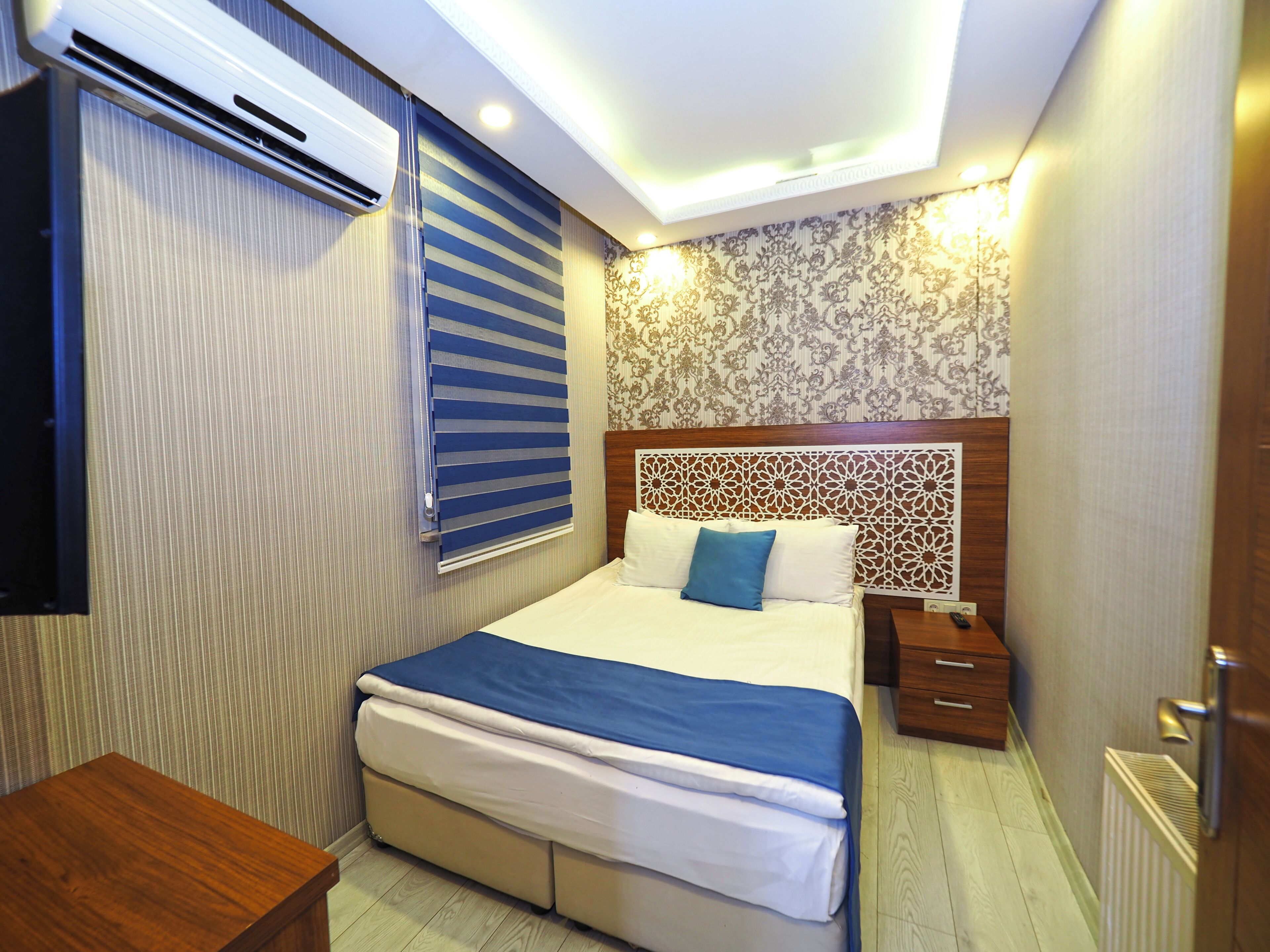 A bedroom with a bed, bedside tables, an air conditioning unit, and a patterned wall.