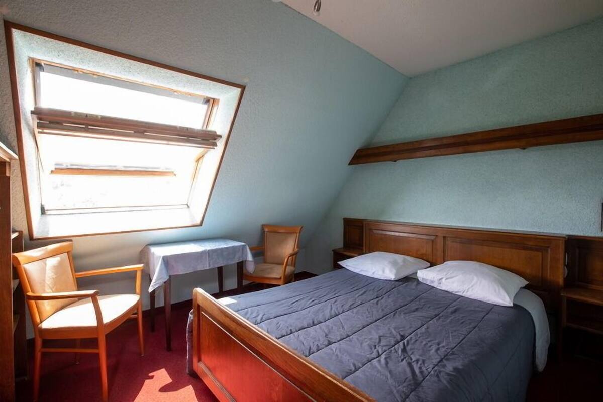 Un dormitorio con cama, una silla, una mesita y una ventana.