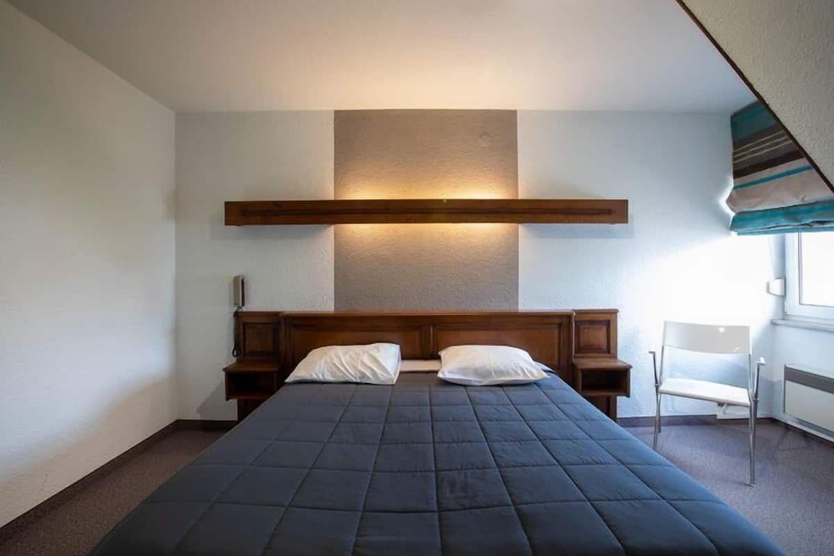 Un dormitorio con una cama, dos mesitas de noche, una silla y un ventanal.