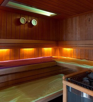 A sauna with wooden walls and benches, a visible thermometer, and a heater. - Hotel Restaurant & Spa Au Tilleul (Labaroche)